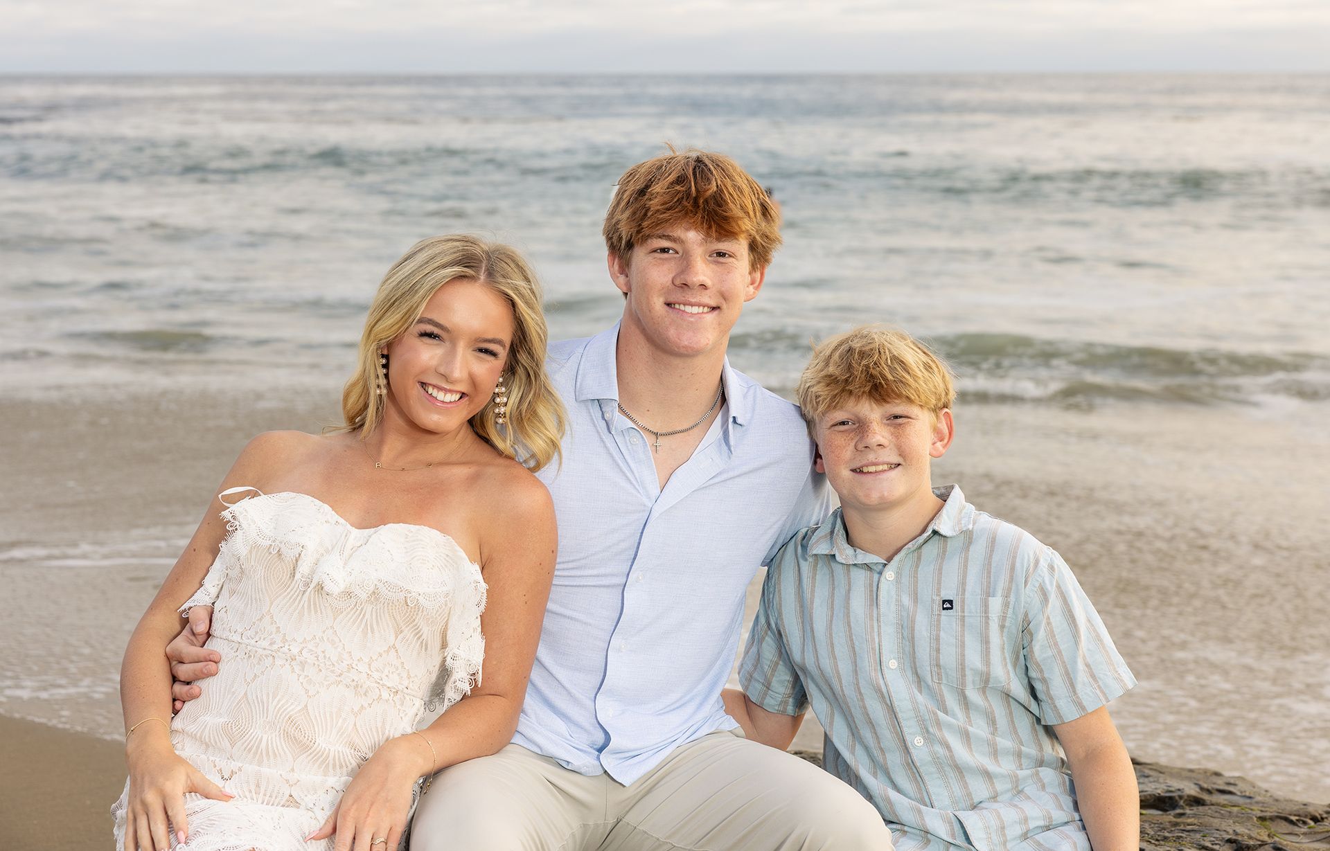 Siblings sitting on a rock at the beach posing for family portraits in Laguna Beach.

