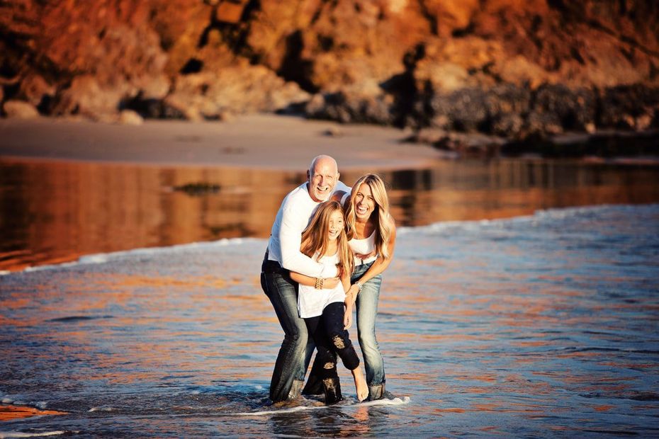 A man and two women are standing in the water on a beach.