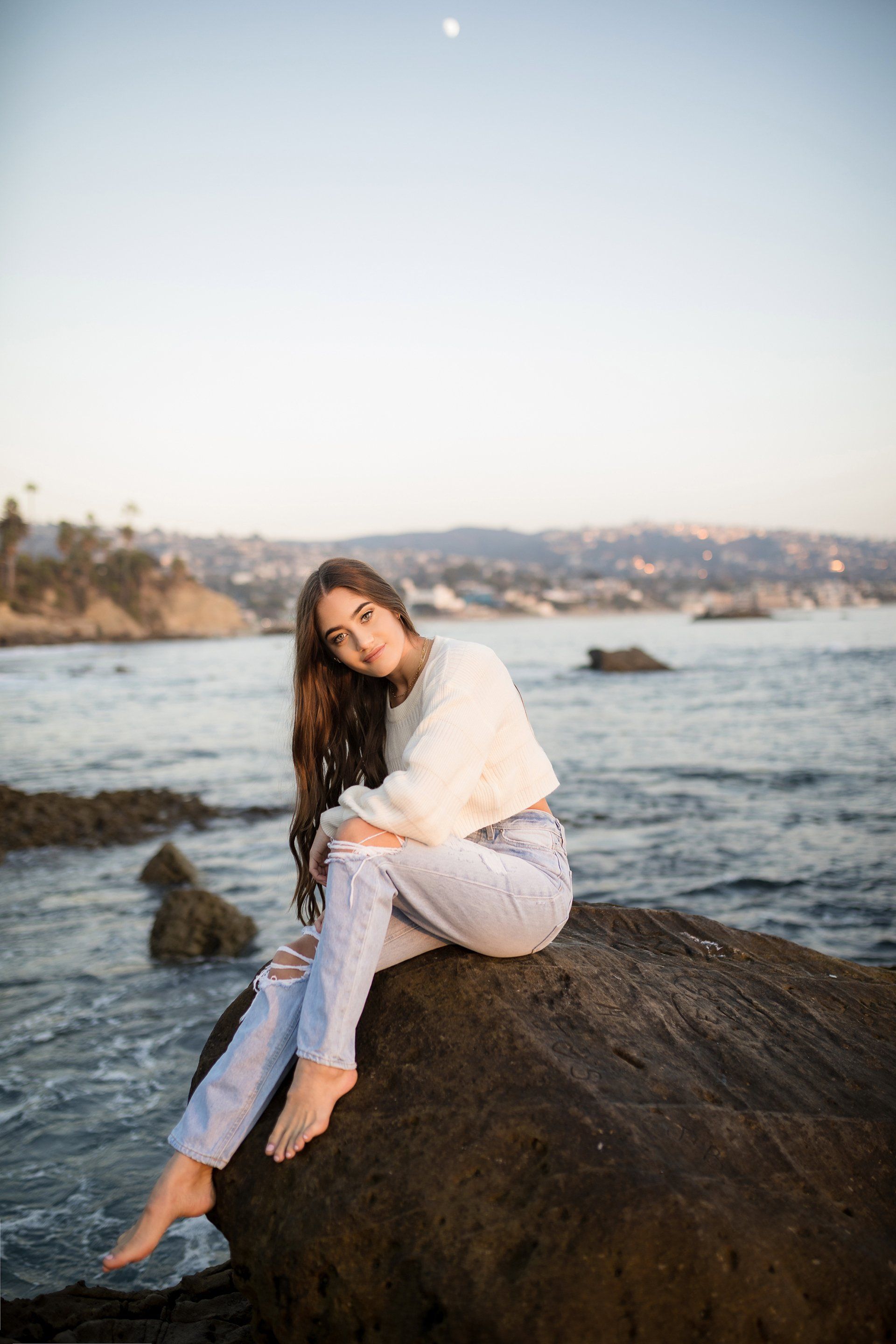 A woman is sitting on a rock near the ocean.