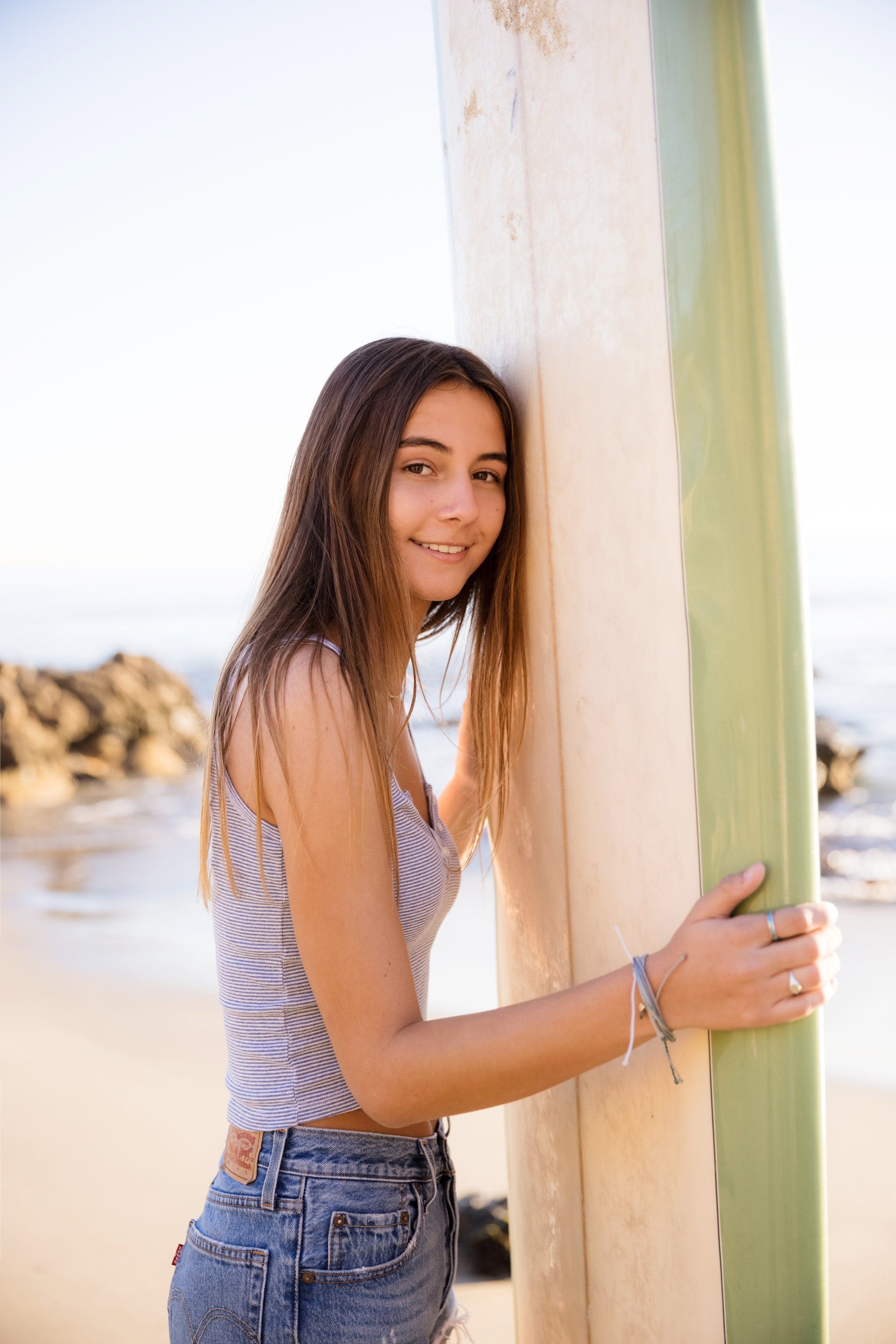 A young woman is leaning against a surfboard on the beach.