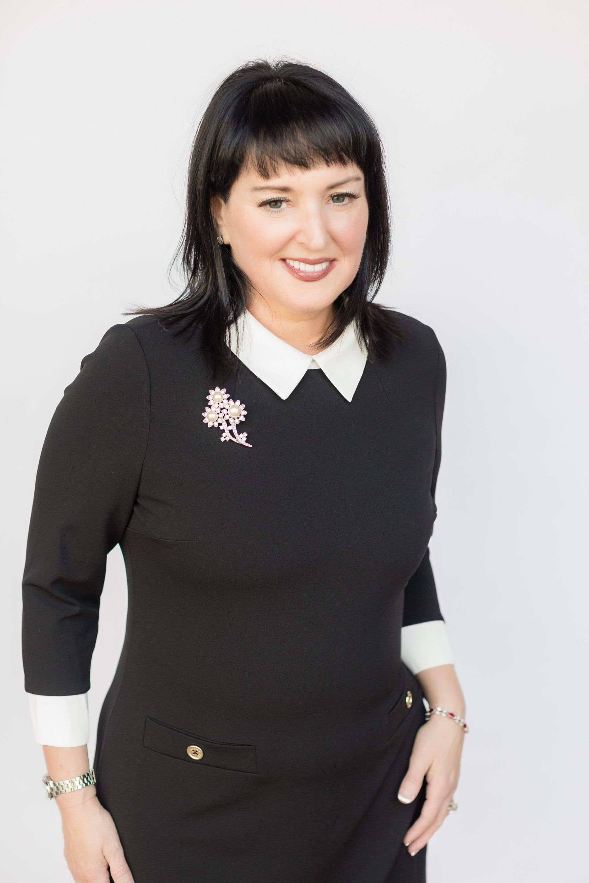 A woman is wearing a black dress and a white collar.