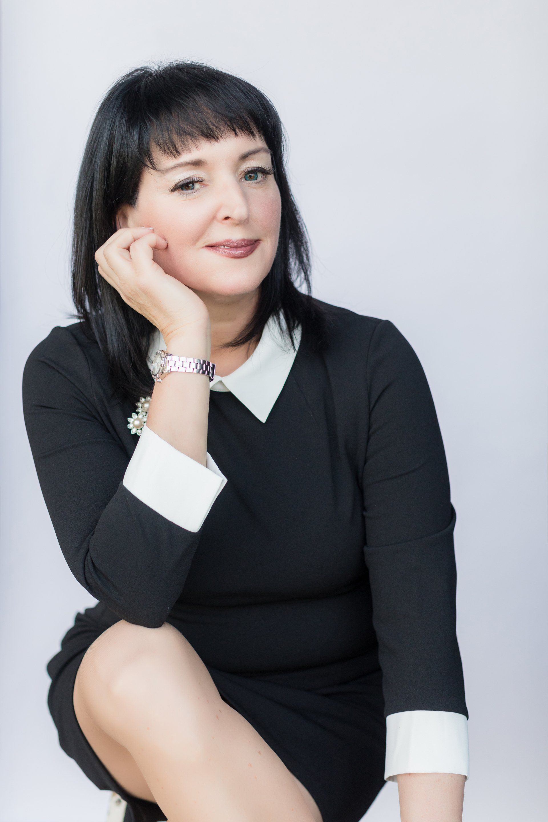 A woman in a black dress is kneeling down with her hand on her chin.