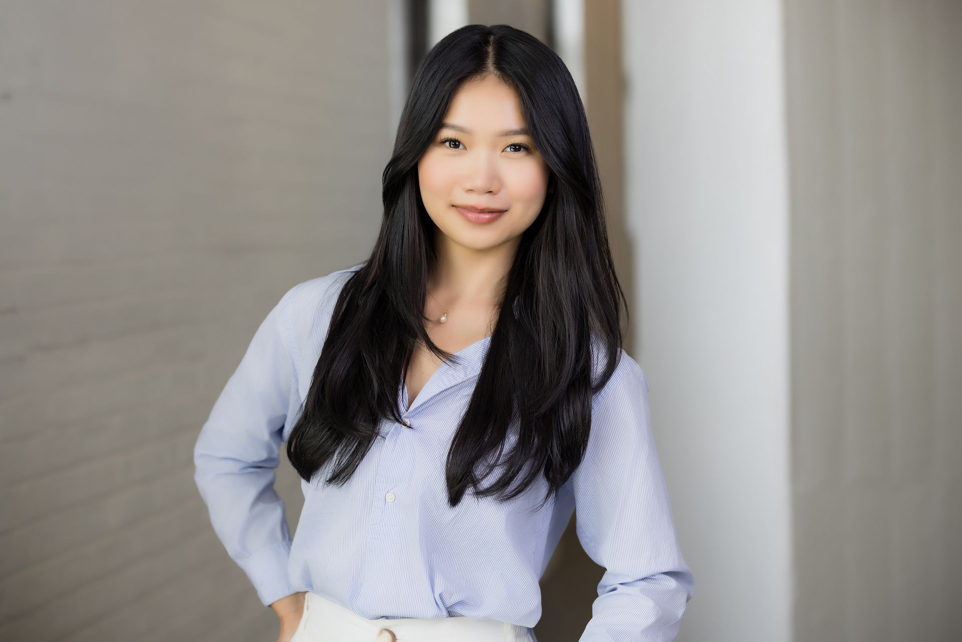 A woman in a blue shirt and white skirt is standing in front of a wall.