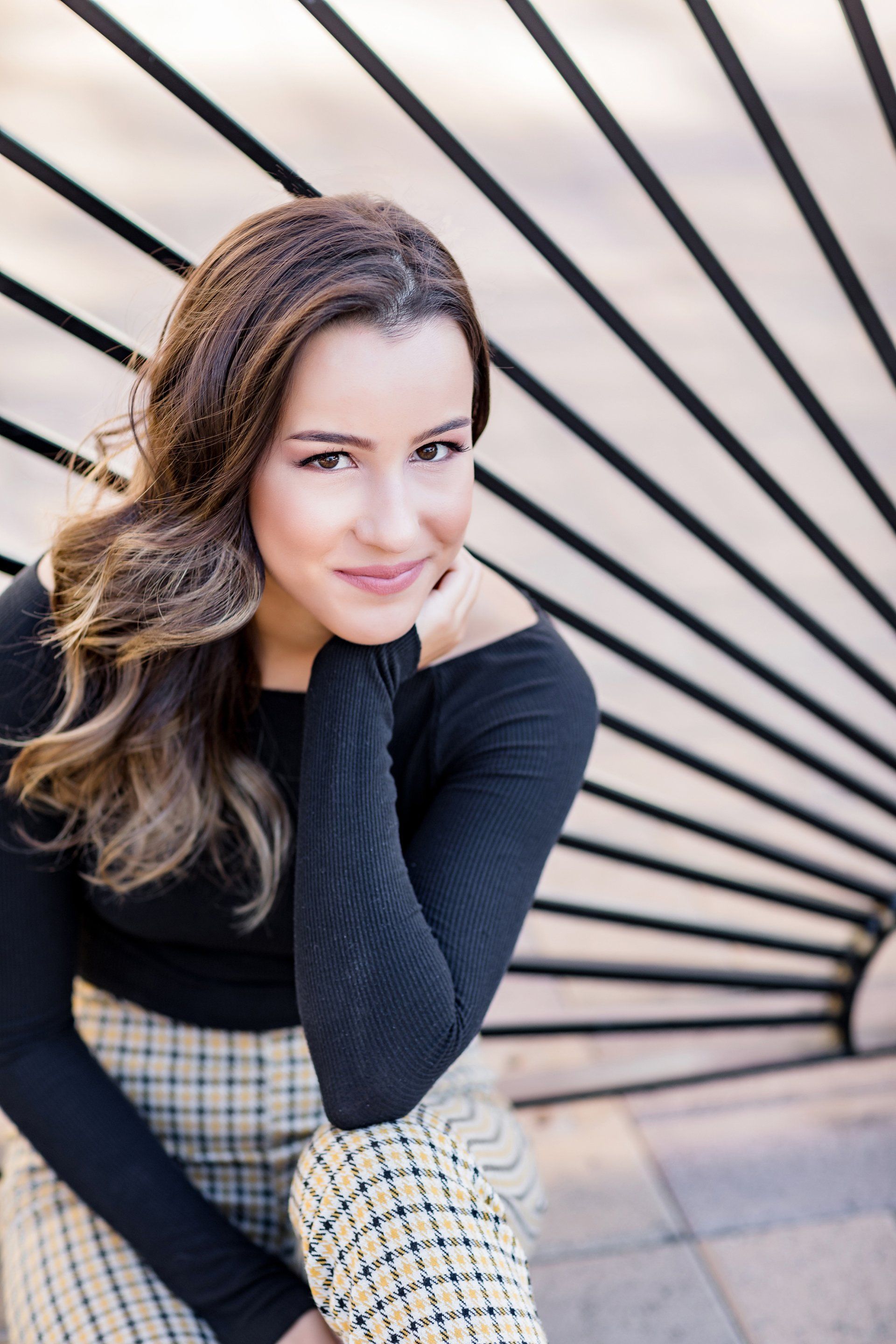 A woman is sitting in front of a fence with her hand on her chin.