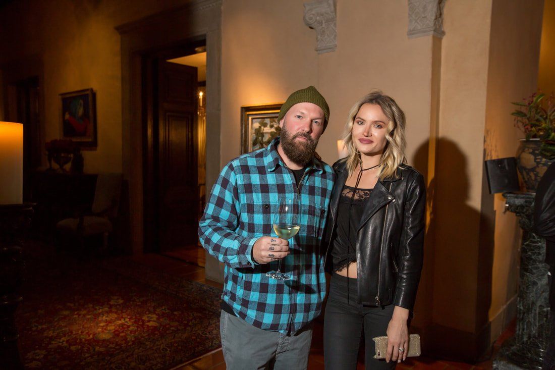 A man and a woman are standing next to each other in a room holding wine glasses.