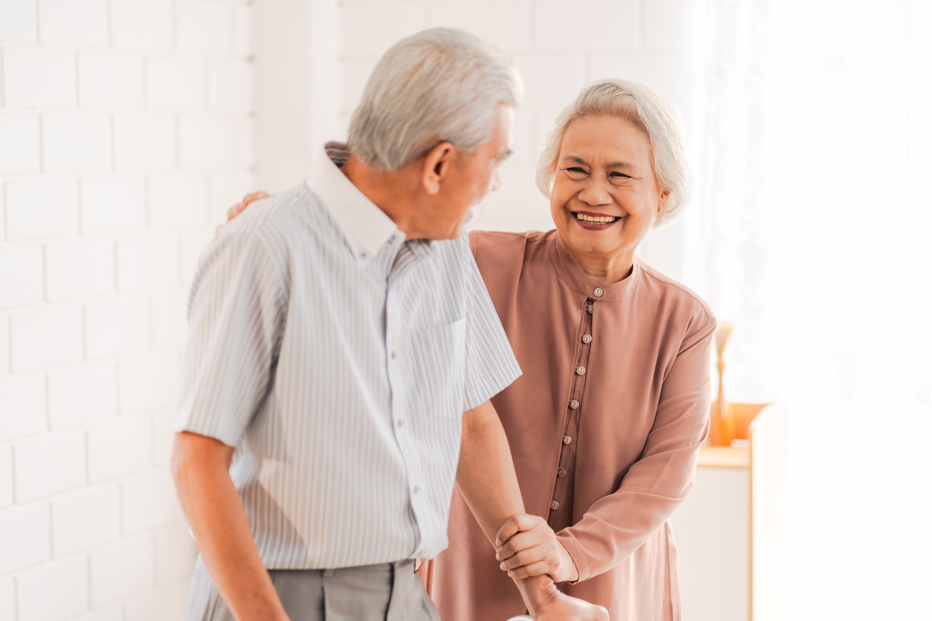 Elderly couple embracing, woman smiling and supporting man. White wall background.
