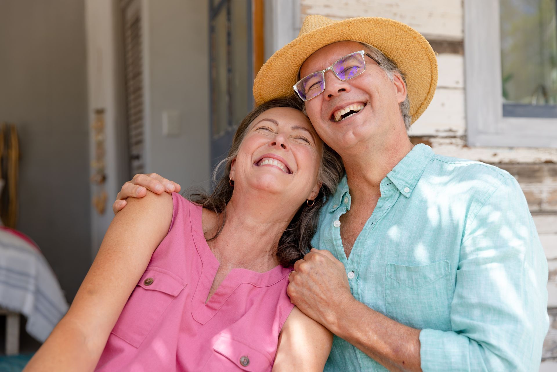 Smiling senior couple outdoors, woman in pink, man in hat, embracing and laughing.