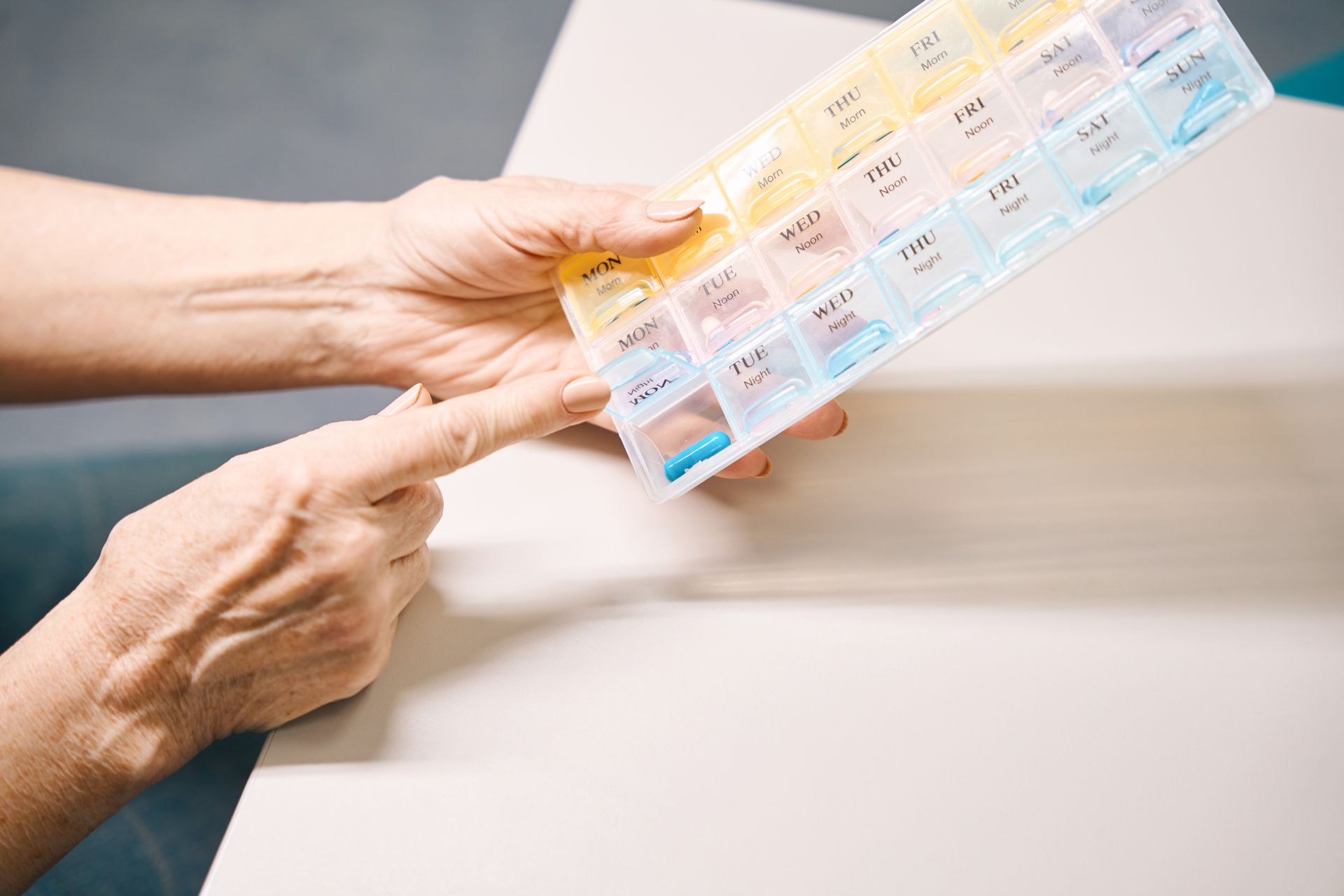 Person's hand pointing to a pill organizer with multiple compartments of medication on a table.