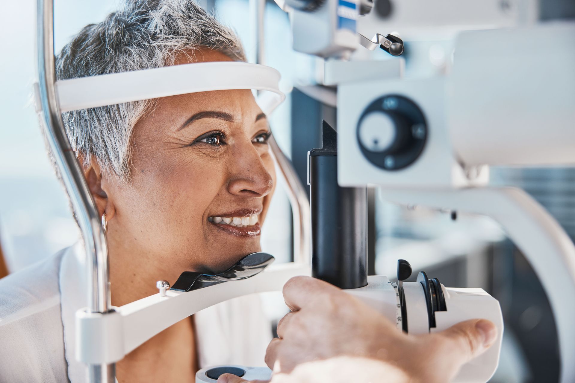 Woman having her eyes examined by an optometrist. She smiles while looking at a machine.
