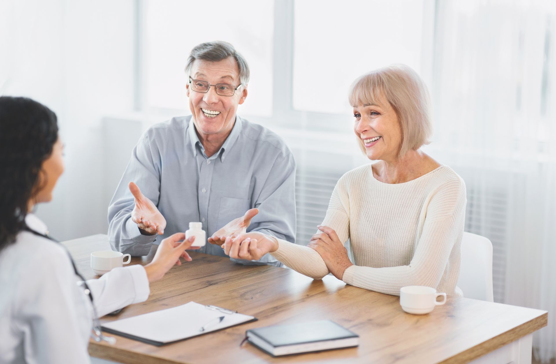 Doctor showing pills to a smiling elderly couple in an office setting.