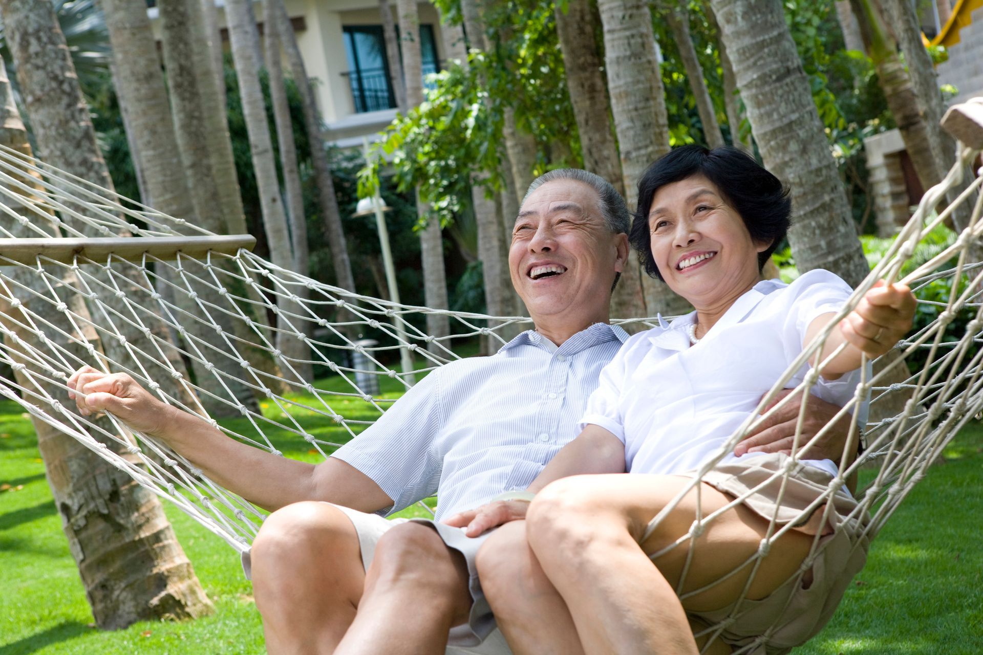 Smiling senior couple relaxes in a hammock outdoors, surrounded by trees.