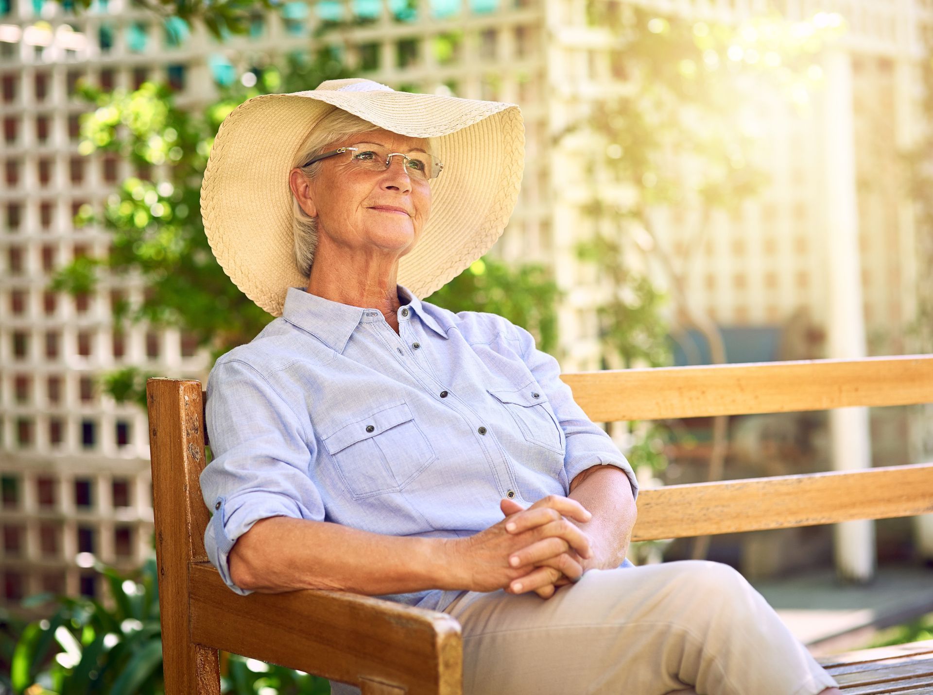 Elderly woman with sunhat, smiling while sitting on a bench outdoors.