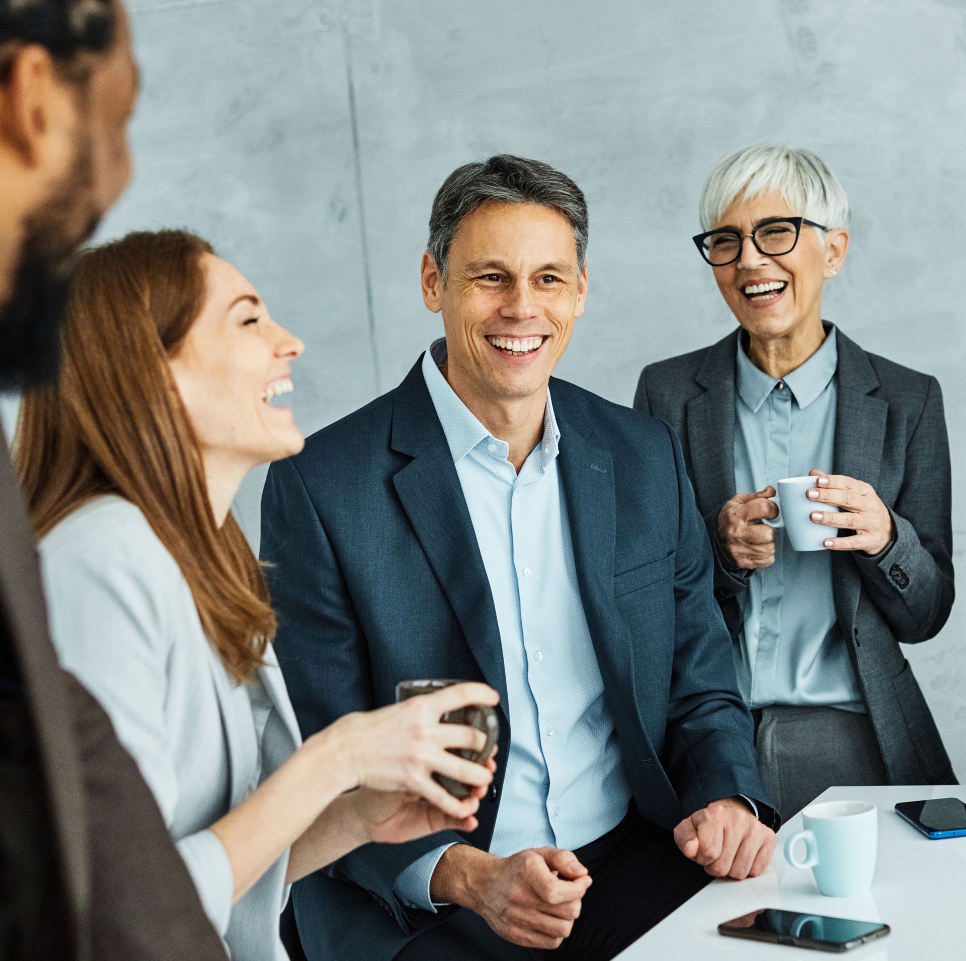 Business colleagues laughing, drinking coffee at a table in a modern office.