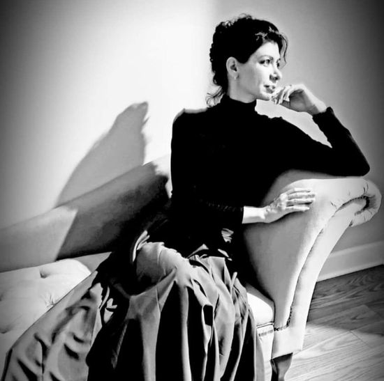 A woman is sitting at a desk with a laptop and a vase of flowers.