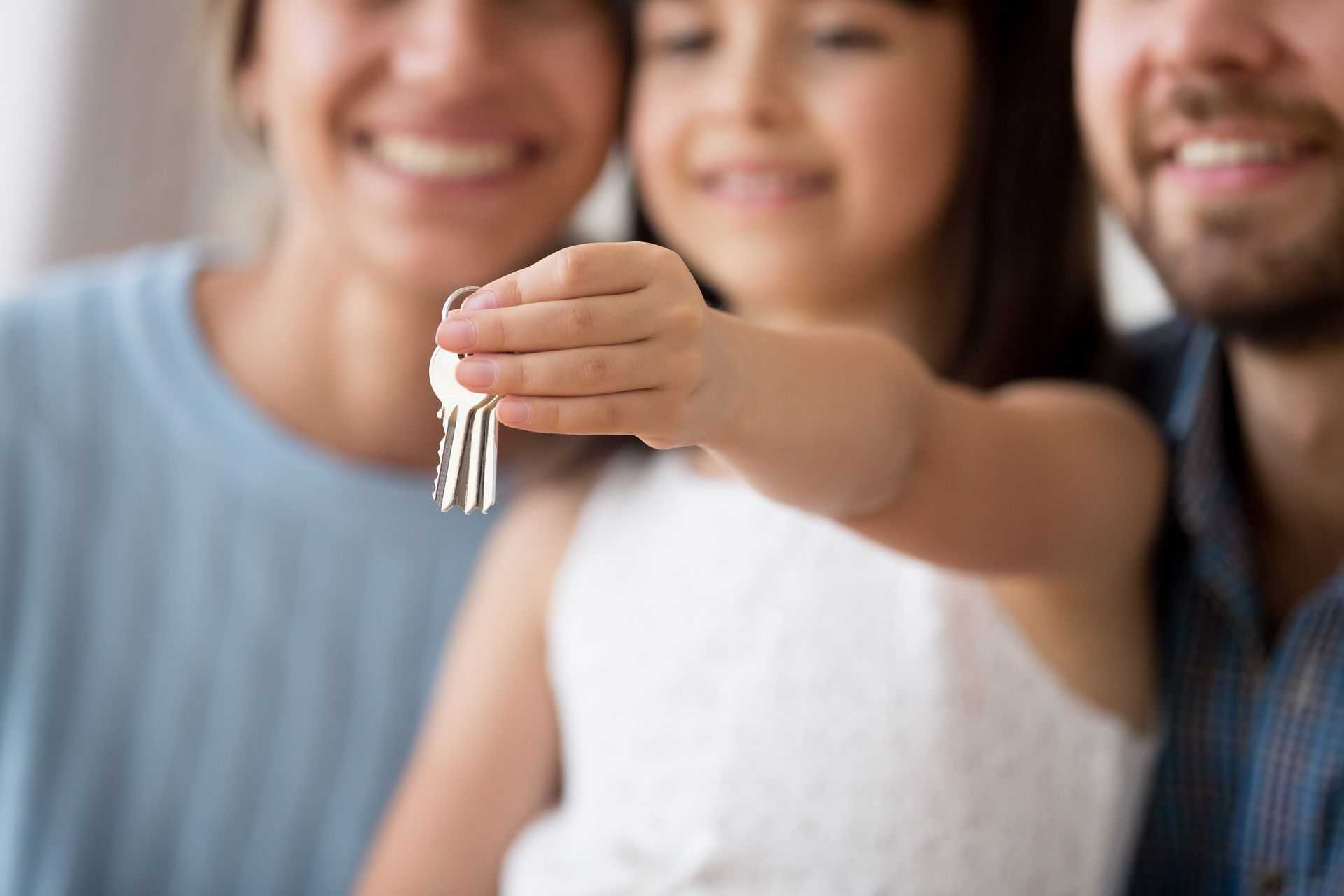 Family, including child, holding keys. Blurred background. Smiling faces.