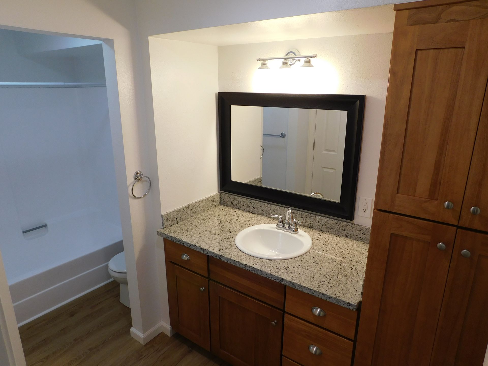 Bathroom with wooden cabinets, granite countertop, white sink, and large mirror.