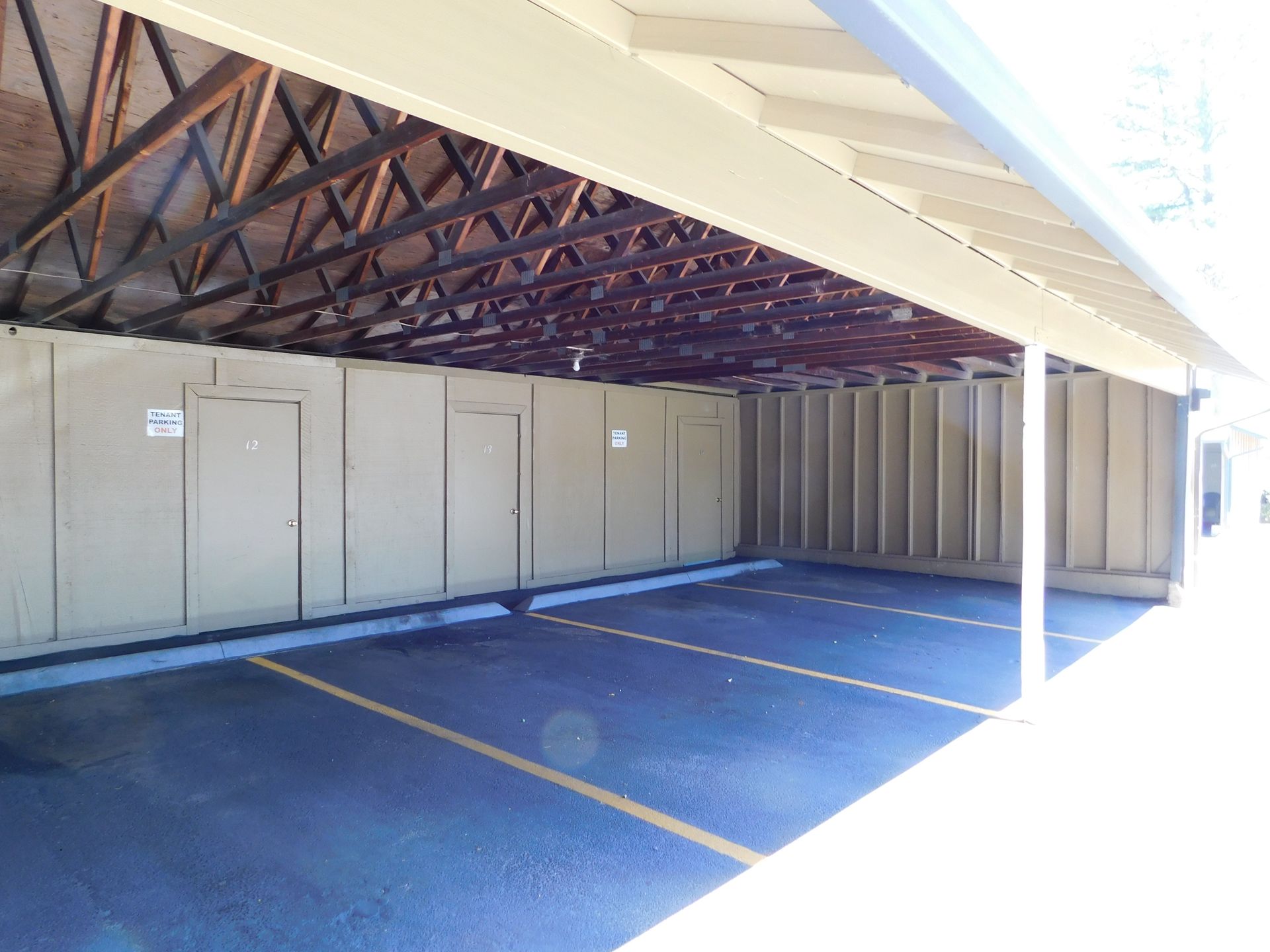 Covered parking area with asphalt and yellow lines, storage doors on the side.