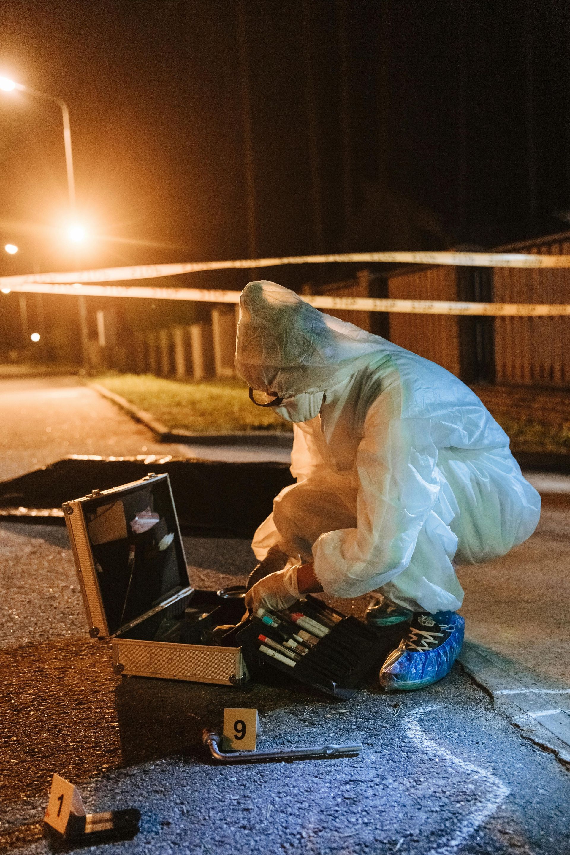 A man in a protective suit is kneeling down next to a briefcase.