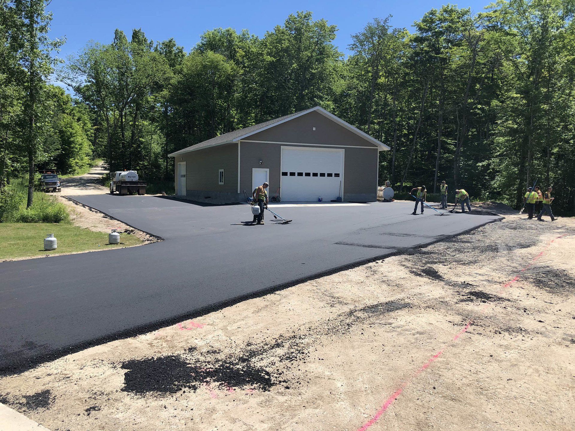 A man is laying asphalt on a driveway in front of a garage.