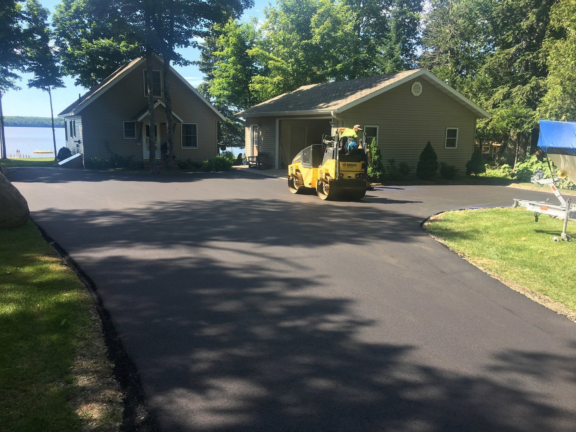 A yellow roller is rolling asphalt in a driveway in front of a house.