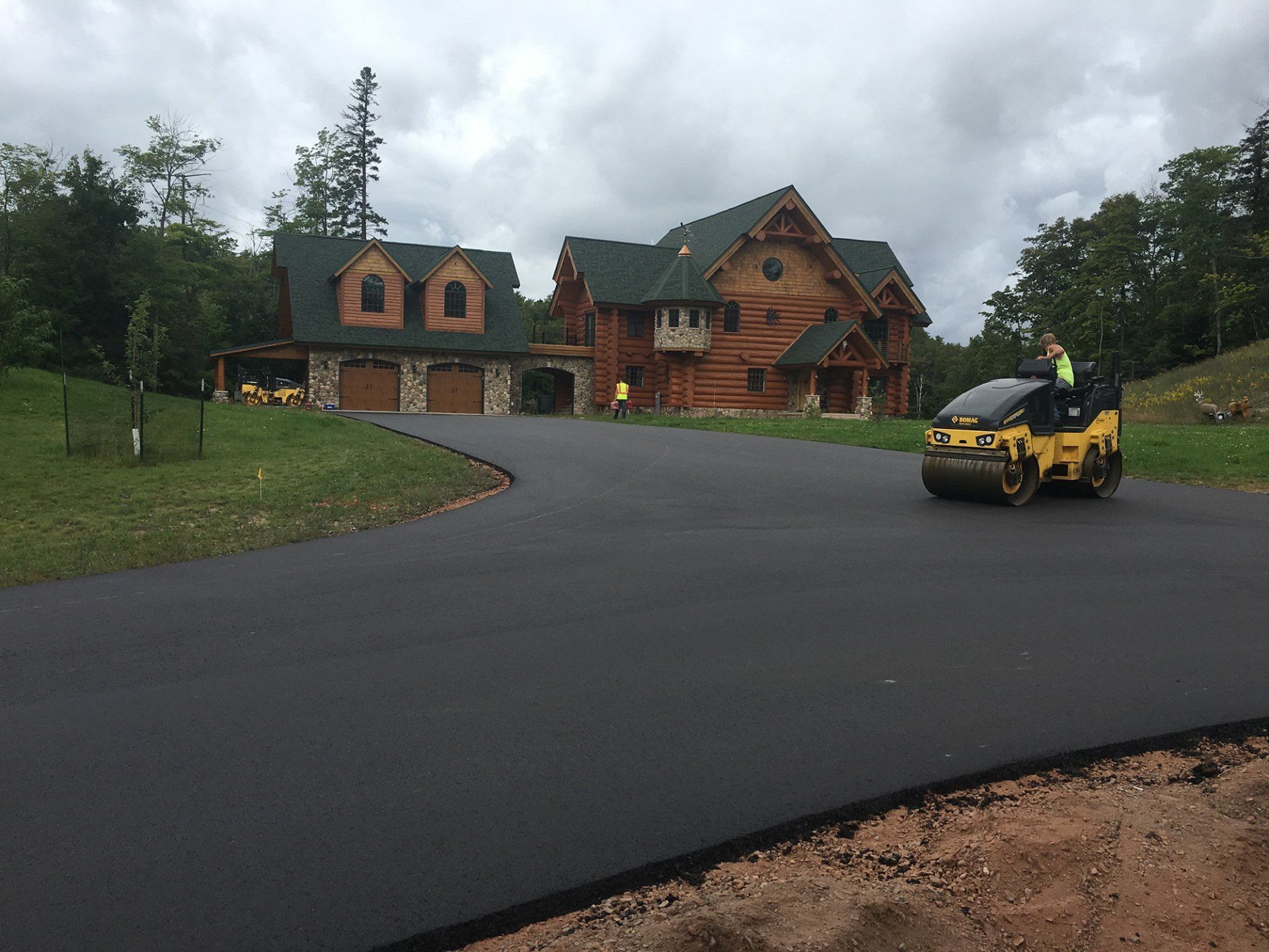A man is driving a roller down a road in front of a large house.