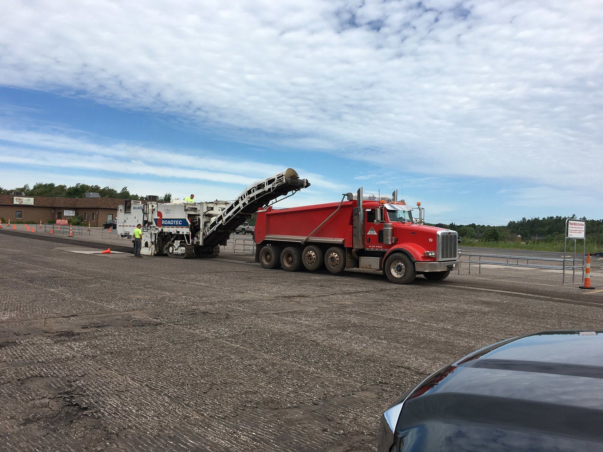 A red dump truck is parked in a parking lot next to a machine.