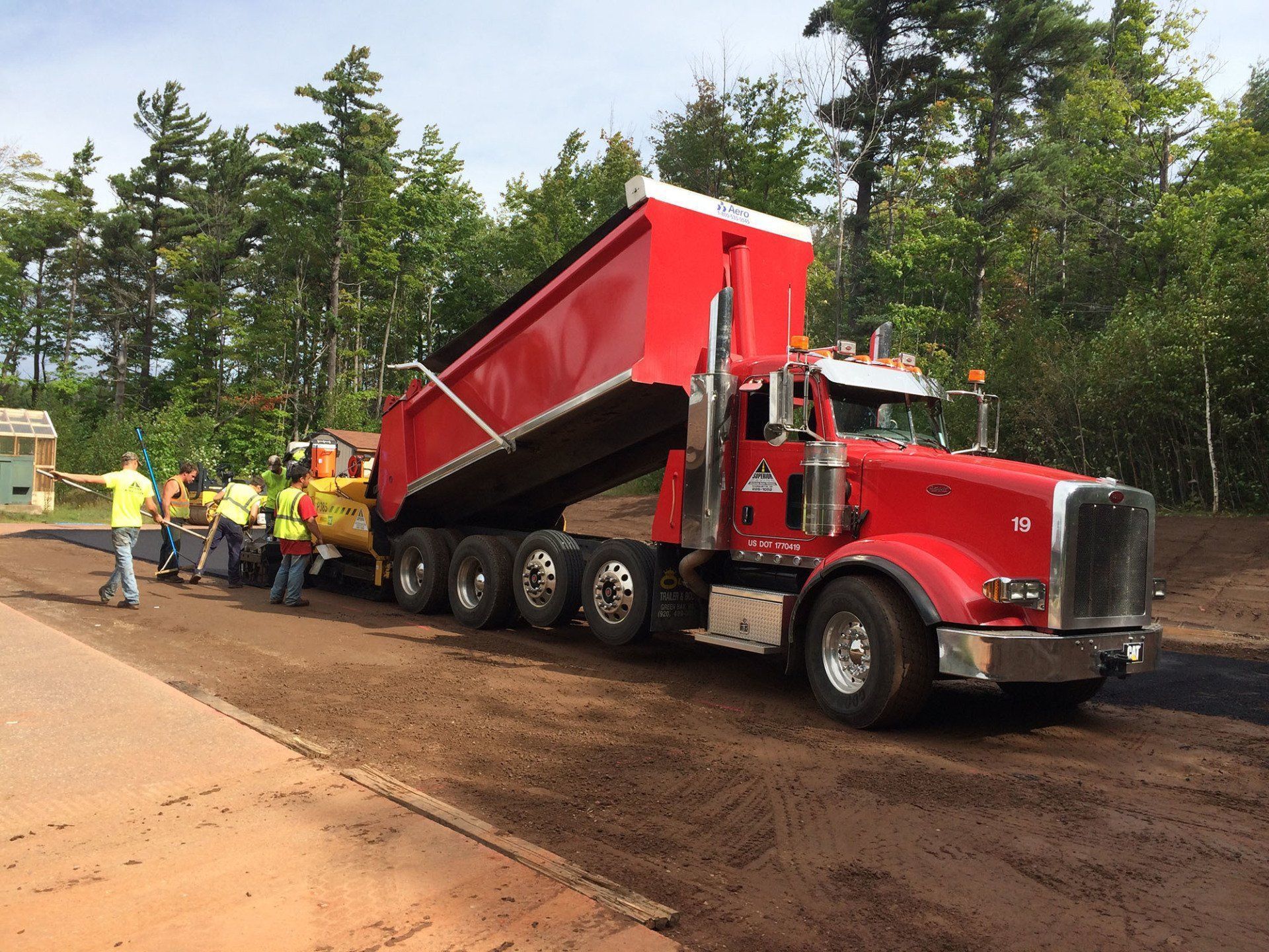 A red dump truck is driving down a dirt road