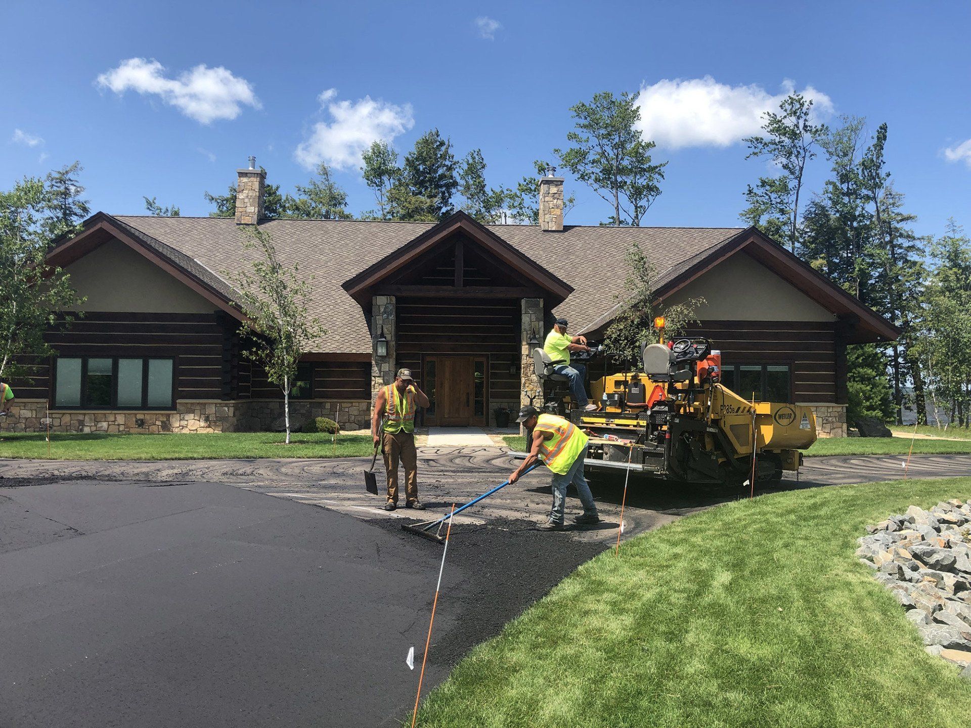 A group of people are working on a driveway in front of a large house.