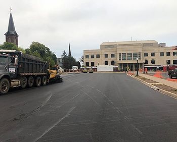 A dump truck is driving down a street in front of a building.