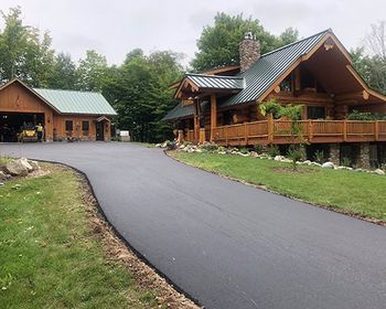 A large log cabin with a driveway leading to it.