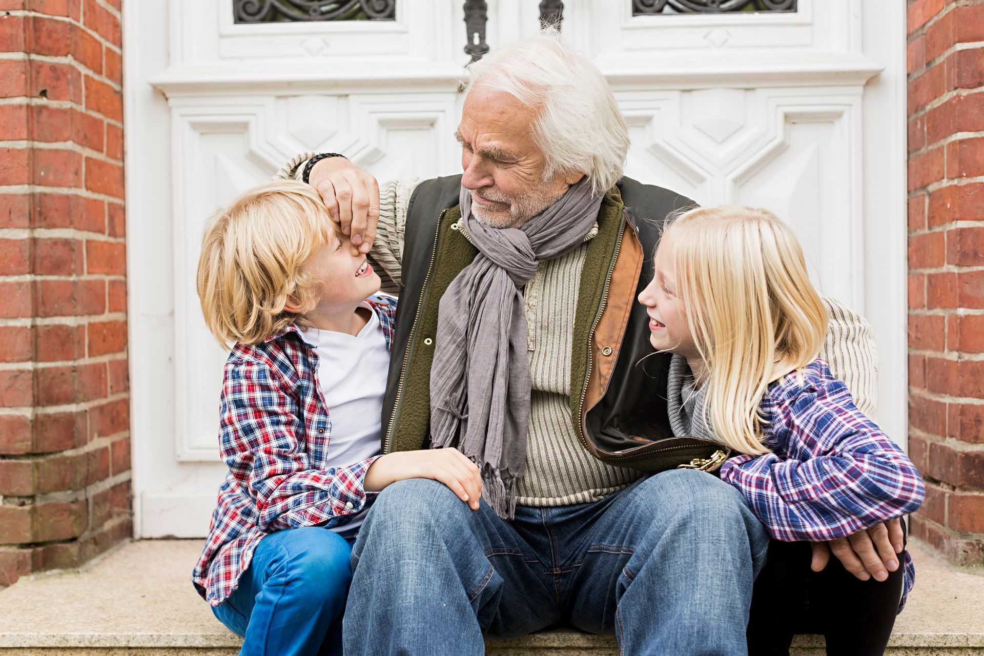 Man sits with two children on steps, touching child's face. Red brick building in background.