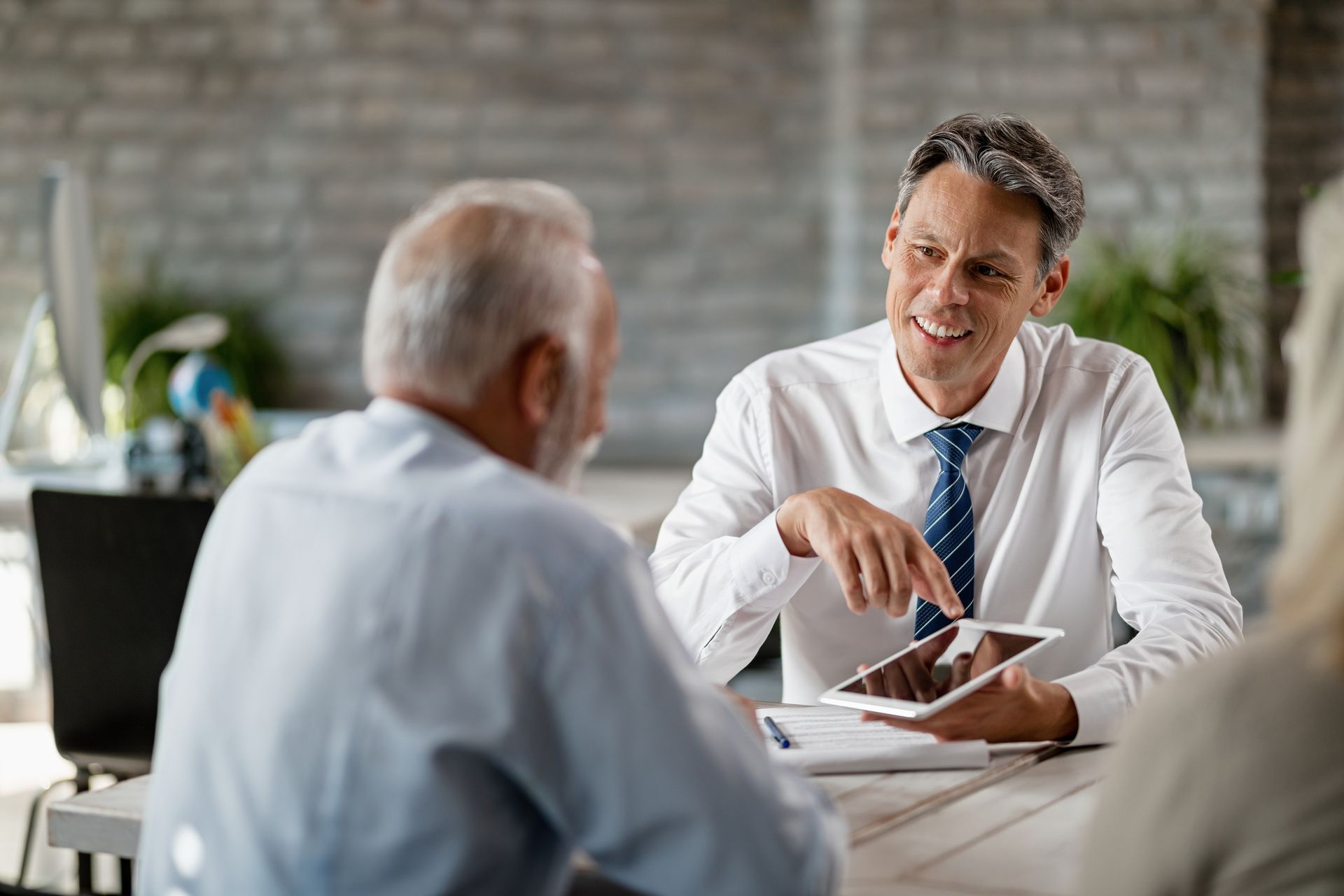 Man pointing at tablet, speaking to older man, in a light-filled office.