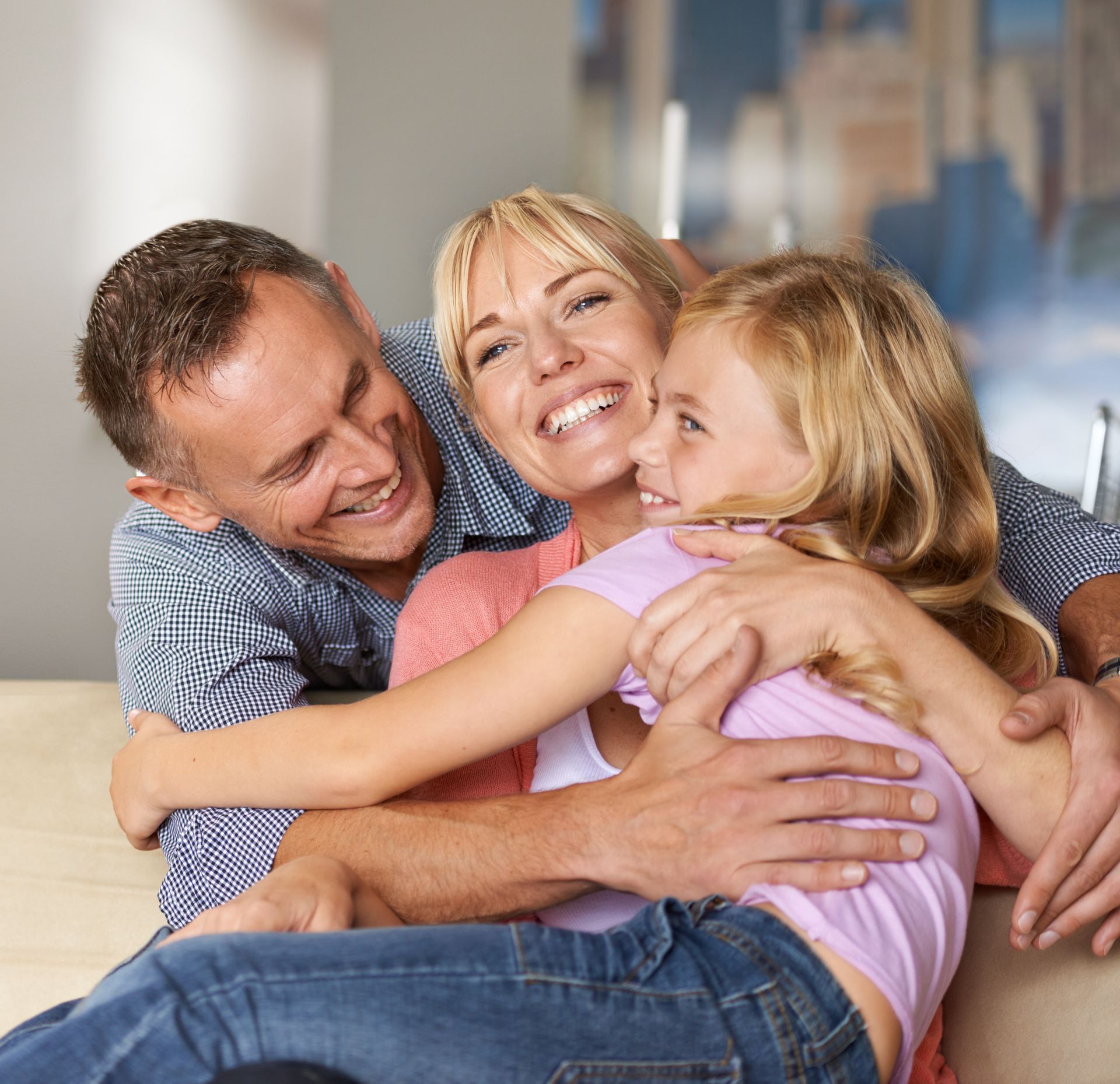 Family hugging, smiling indoors. Mother, father, and daughter embracing joyfully.