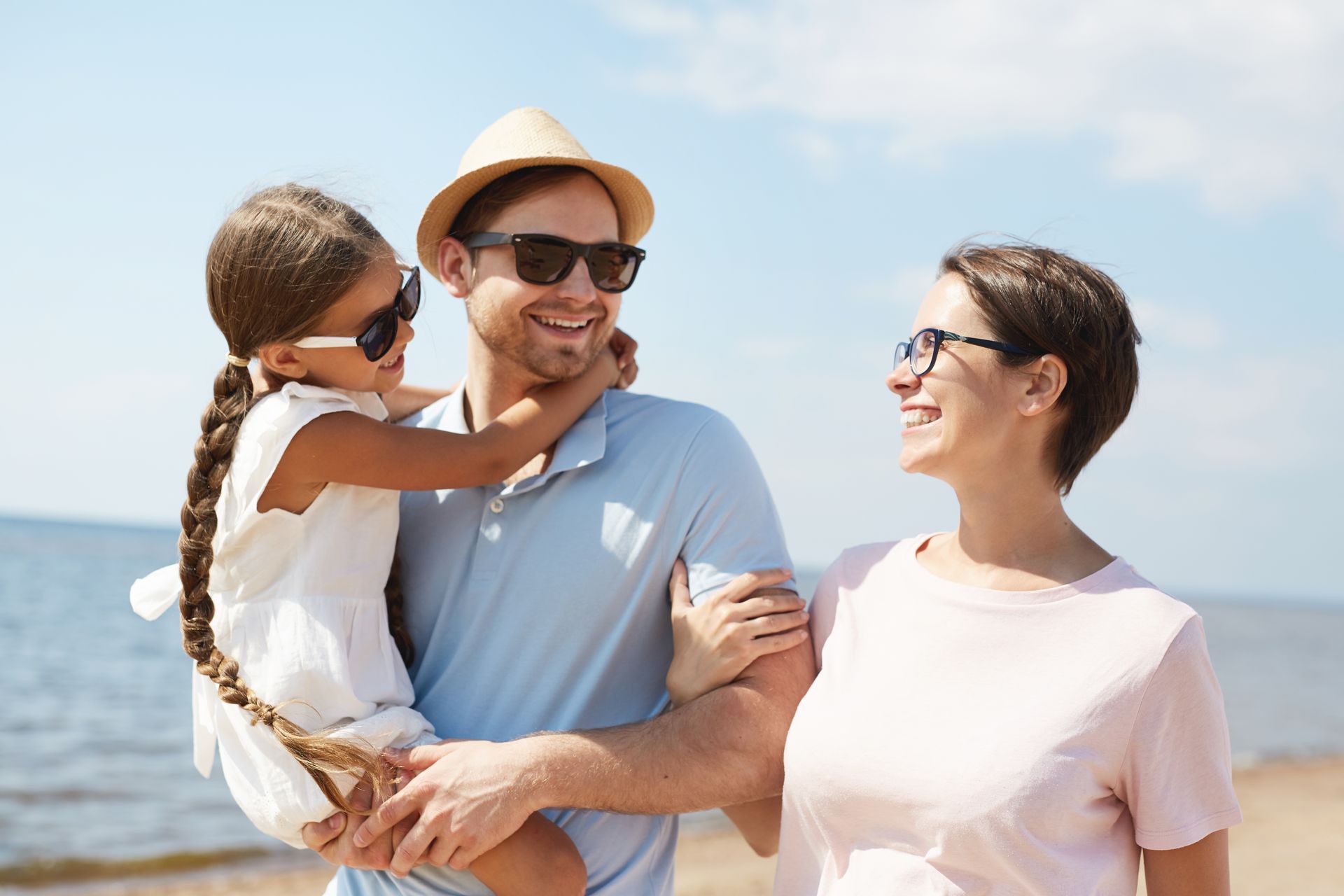 Family of three smiling at the beach; father holding child, mother beside them.