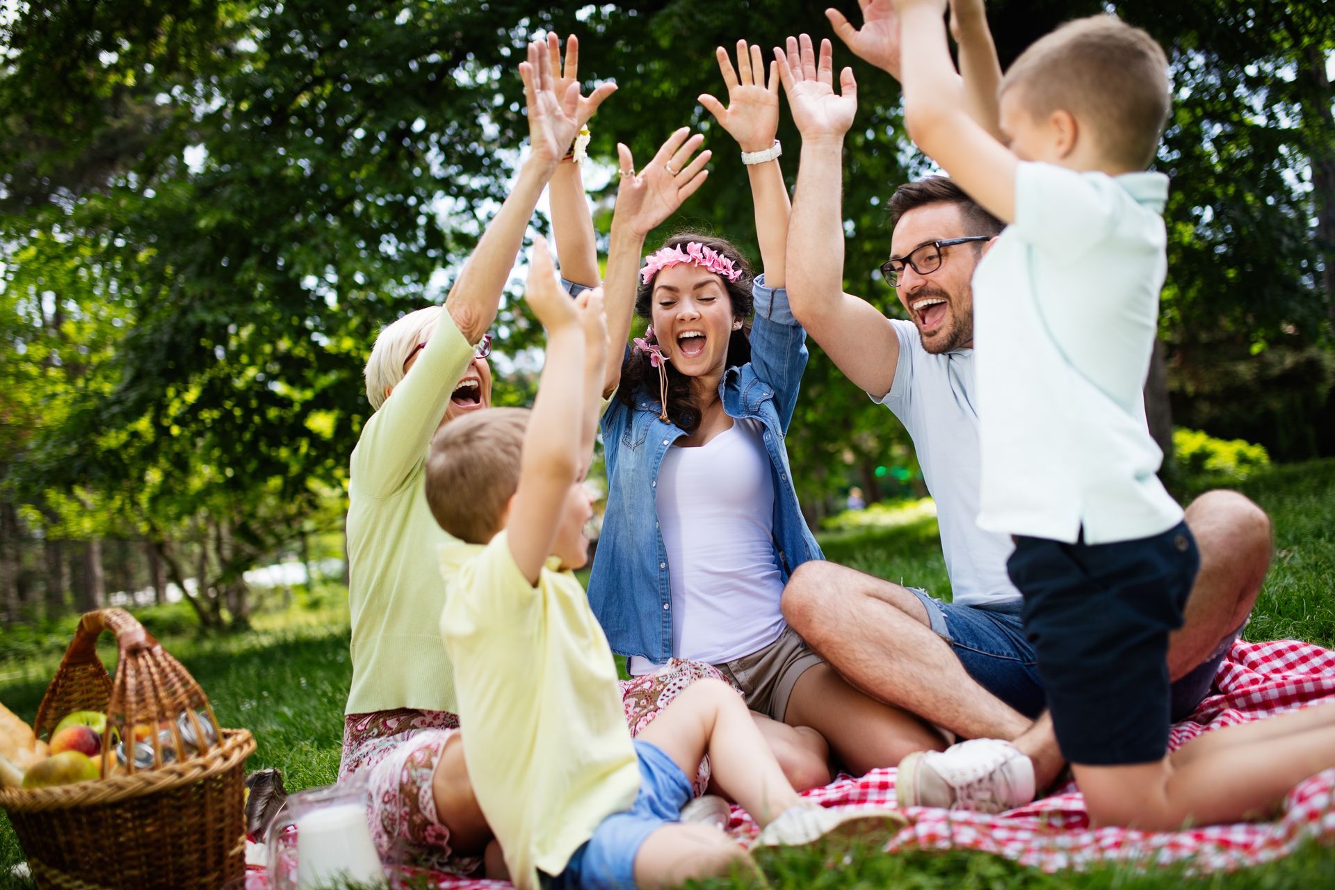 Family picnic with outstretched arms celebrating on a red and white blanket in a park.