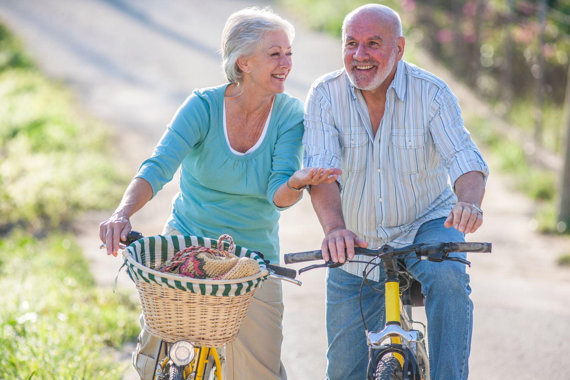 Smiling couple riding bicycles on a paved path, woman pointing, basket on front bike.