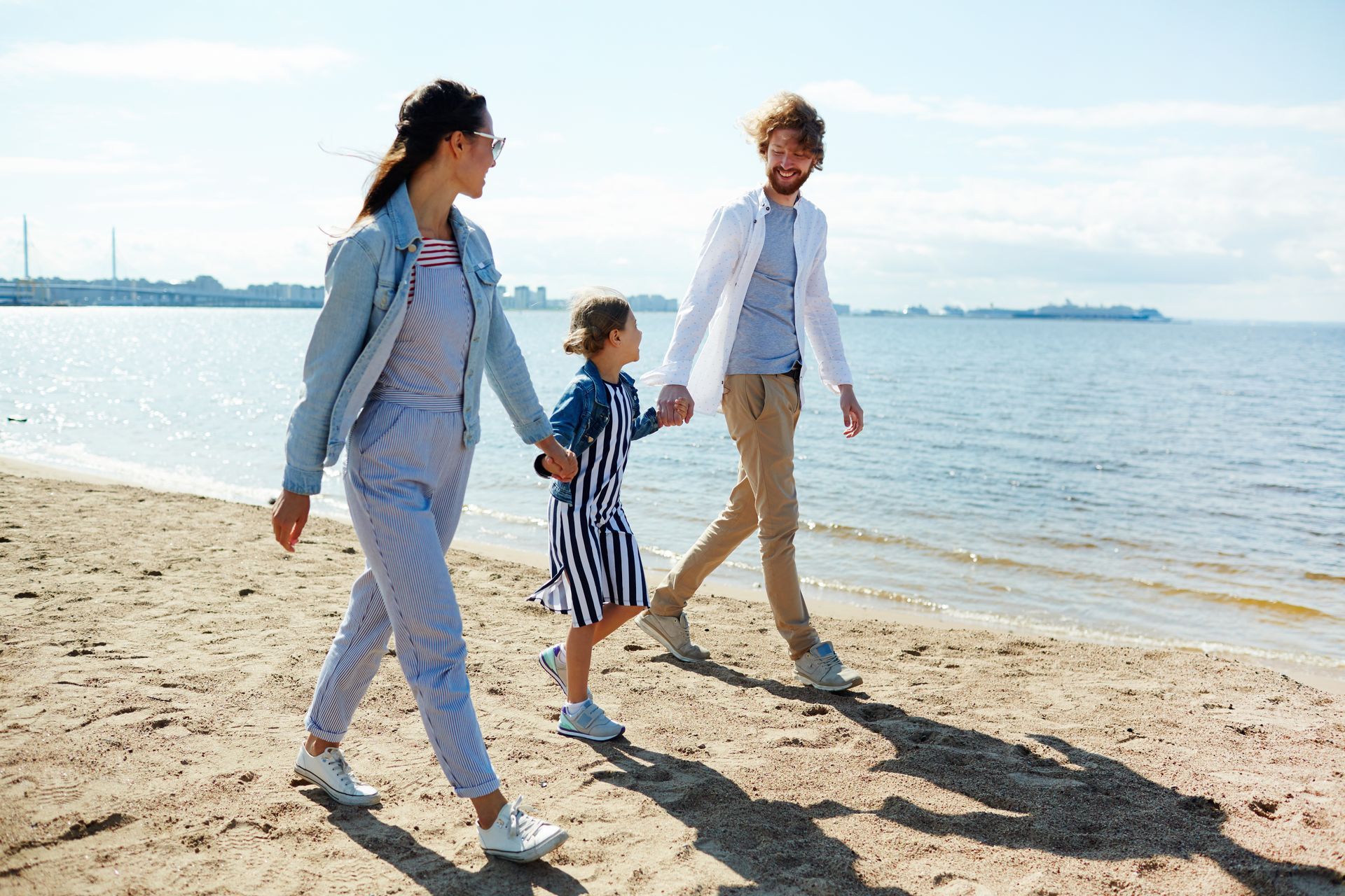 Family walking on a sandy beach. Holding hands, smiling, sunny day.