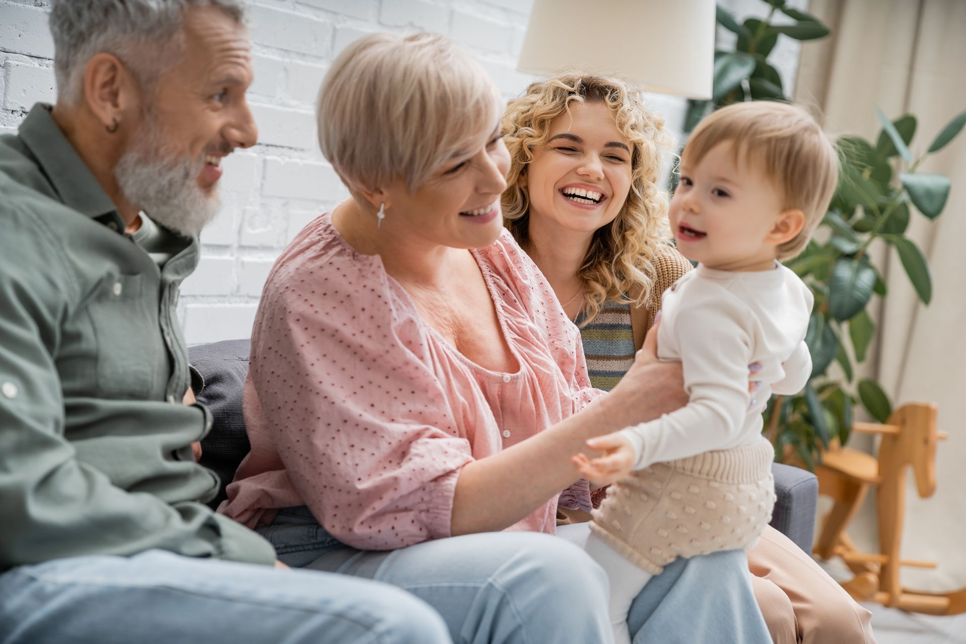 Family with baby smiling on a sofa; grandparents, mother and child in living room.