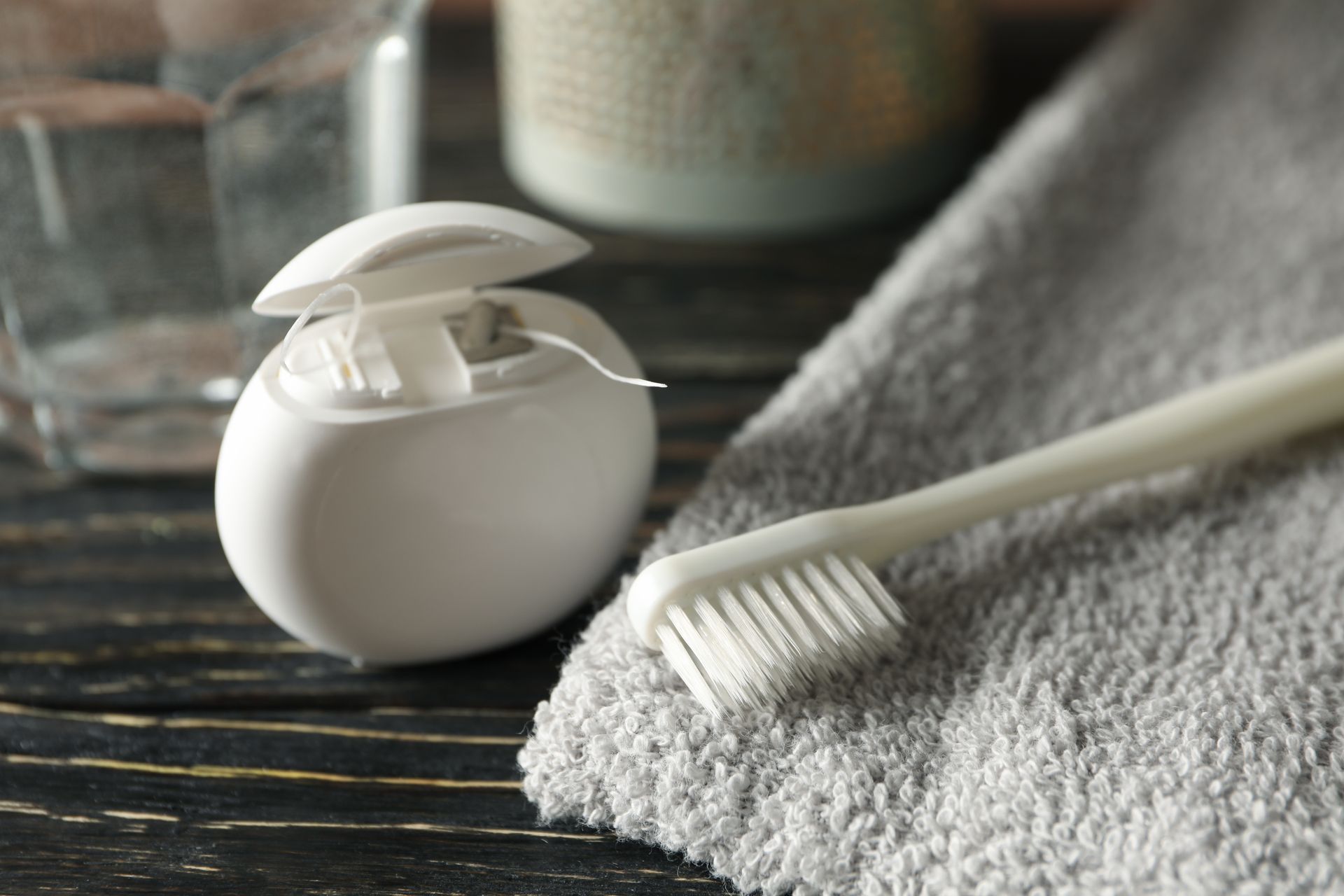 Dental floss, toothbrush, and towel on a dark surface, representing dental hygiene.