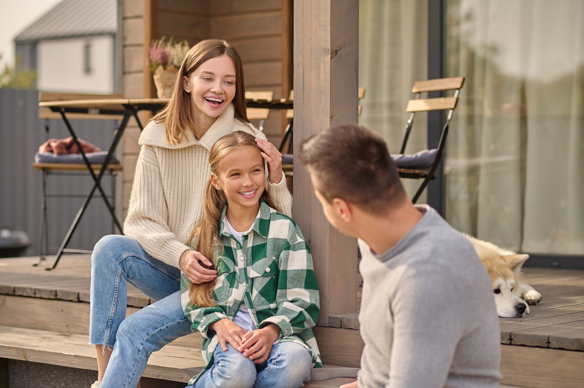 Family sitting on a porch, smiling. A dog rests nearby.
