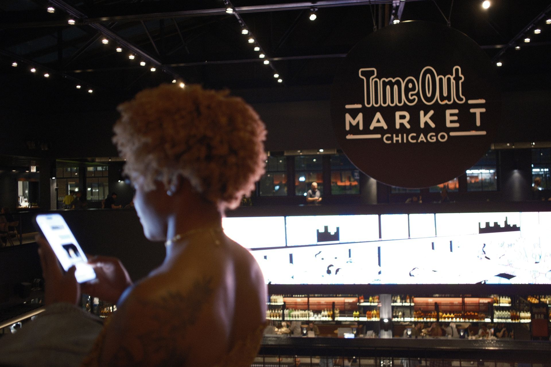 A woman is looking at her phone in front of a timeout market sign