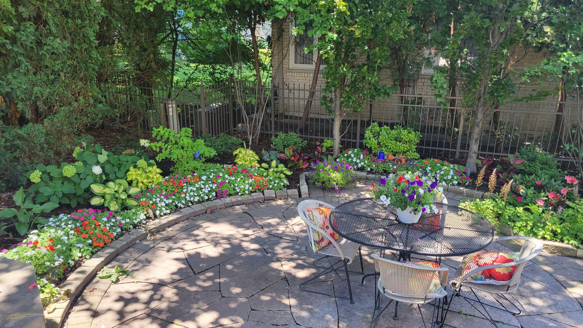 A patio with a table and chairs in the middle of a garden.