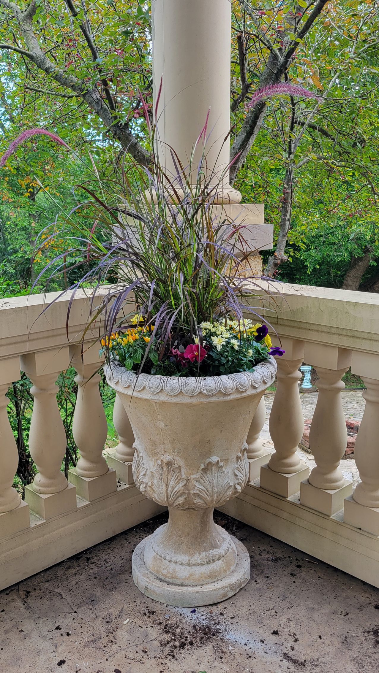 A large vase filled with flowers is on a balcony.