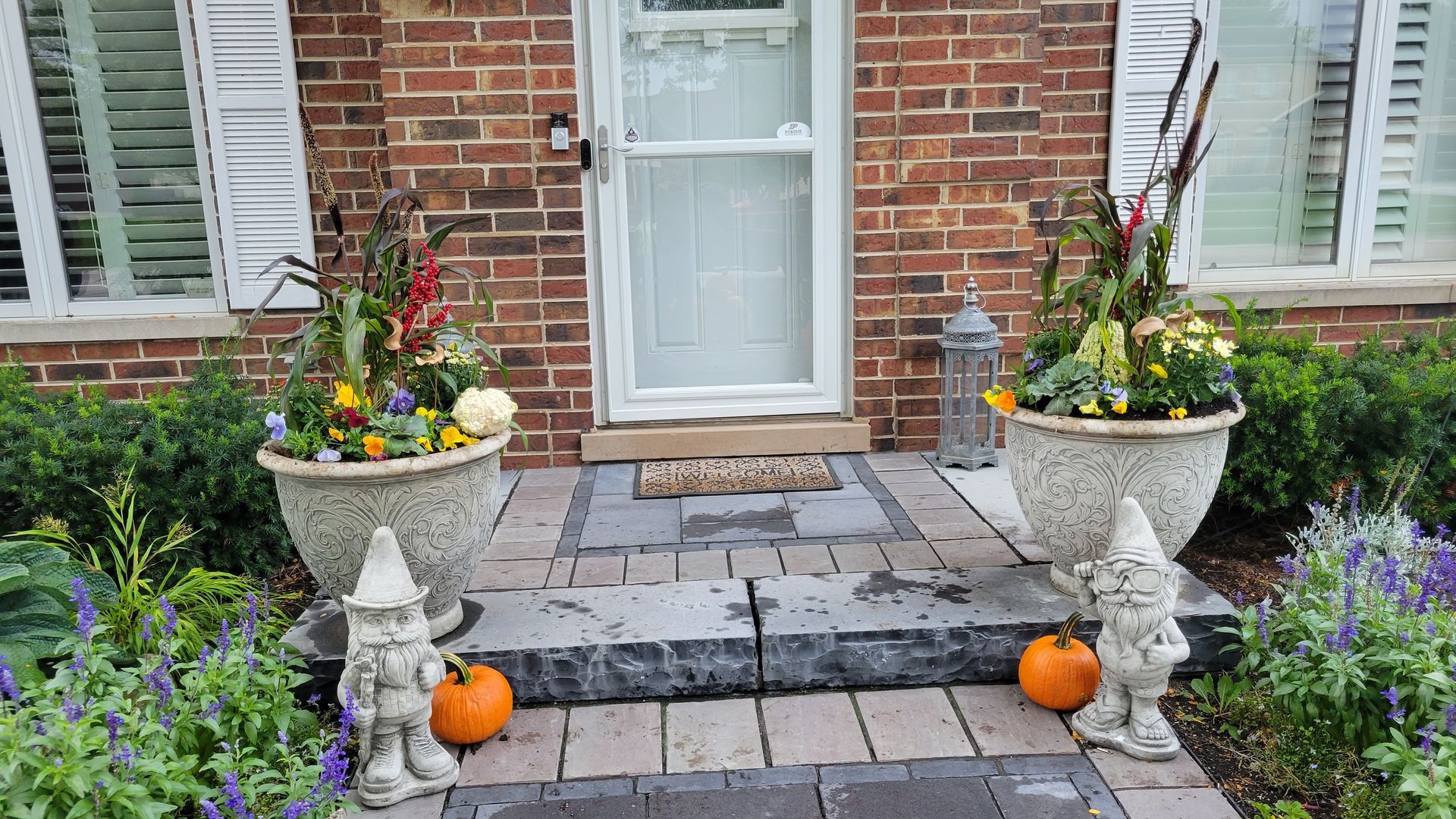A brick house with a porch decorated for halloween with pumpkins and gnomes.