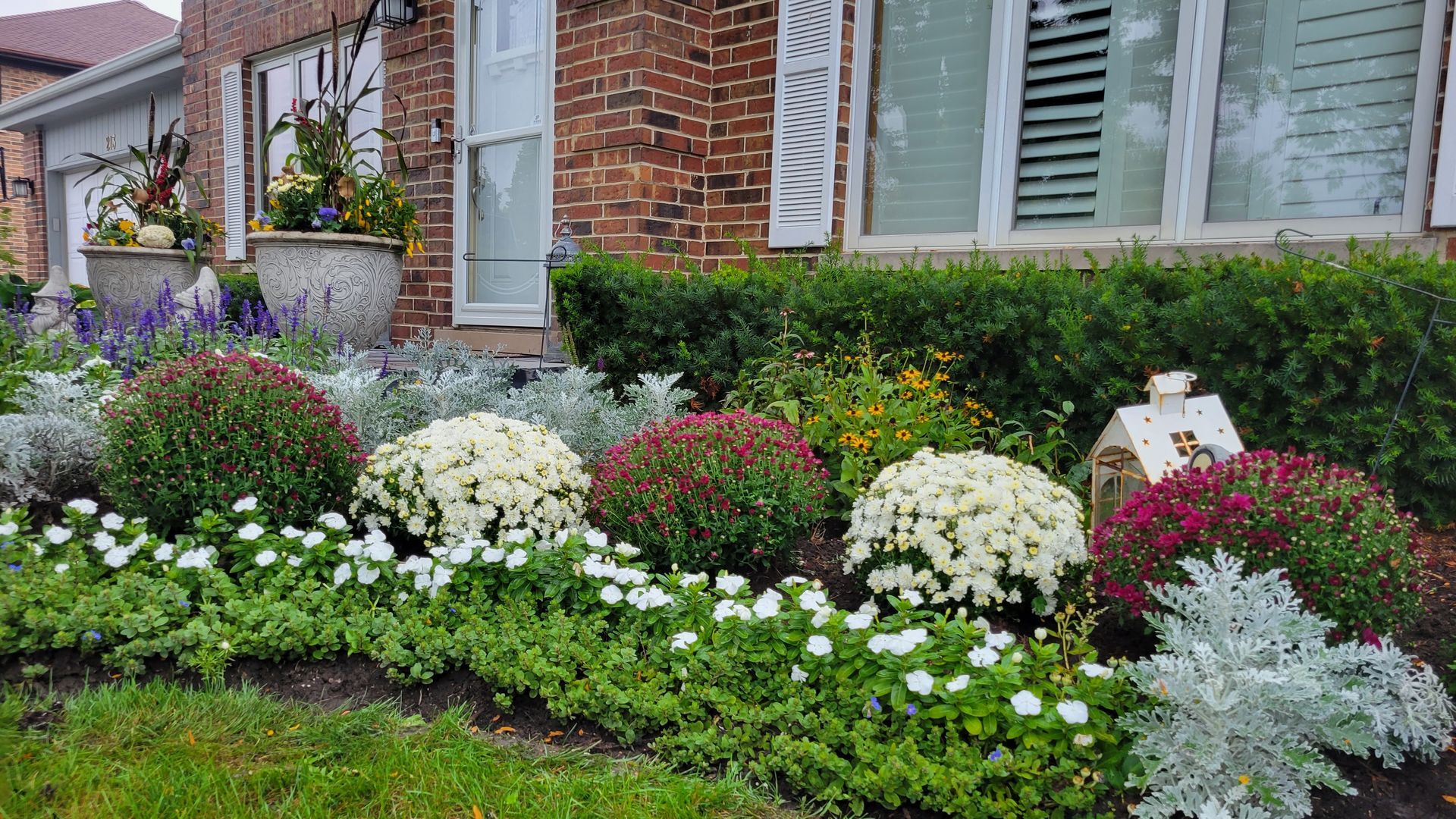 A garden with lots of flowers and plants in front of a brick house.
