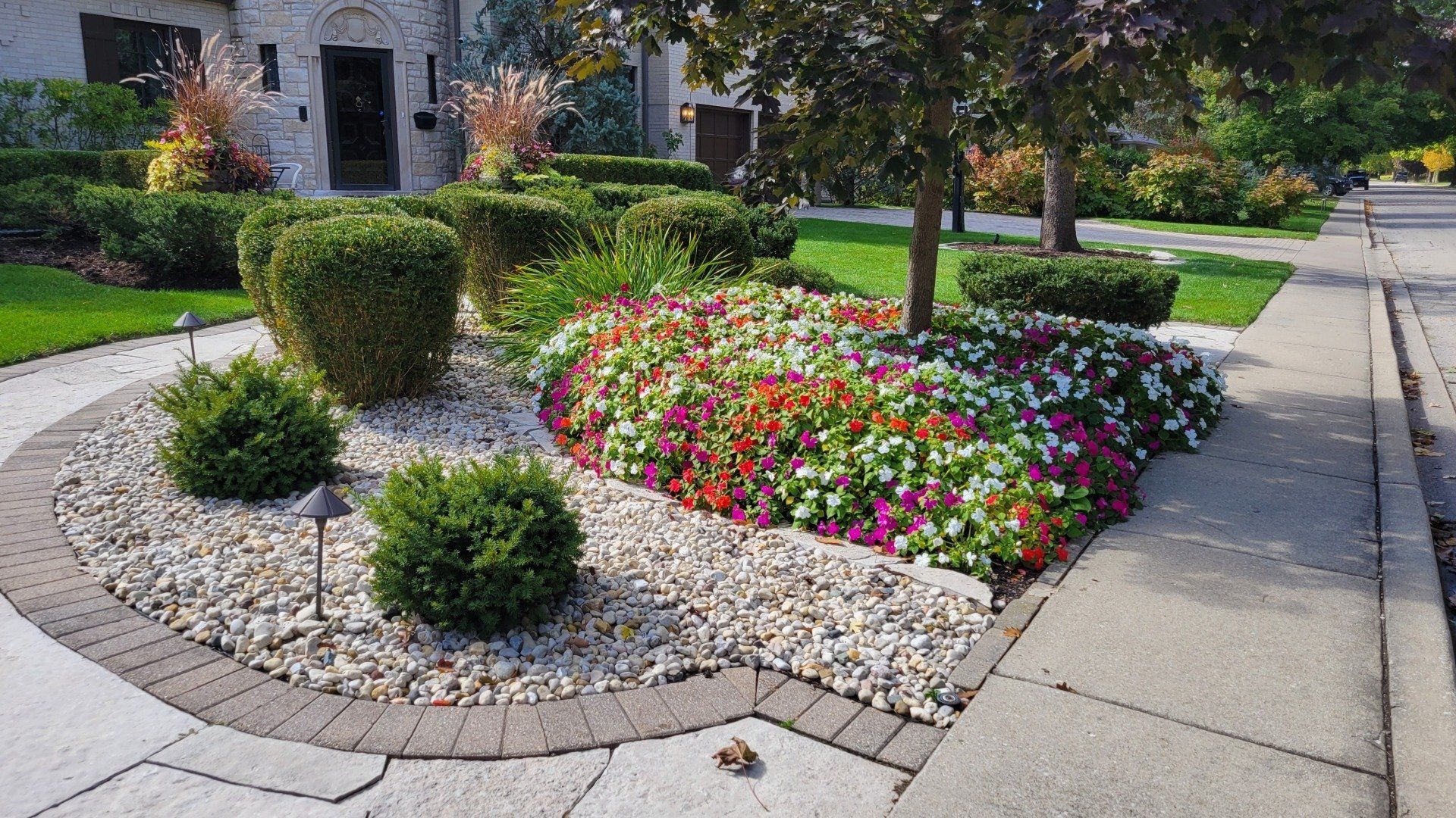 A garden with flowers and rocks on the sidewalk in front of a house.