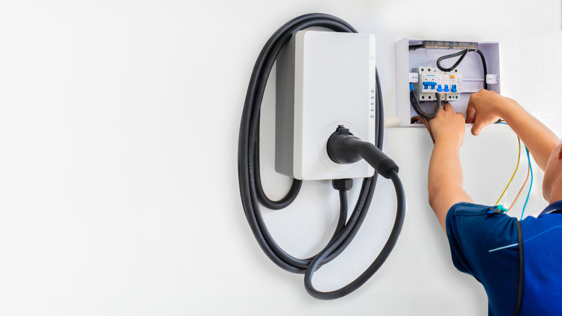 Person installing EV charger on white wall, wiring exposed.
