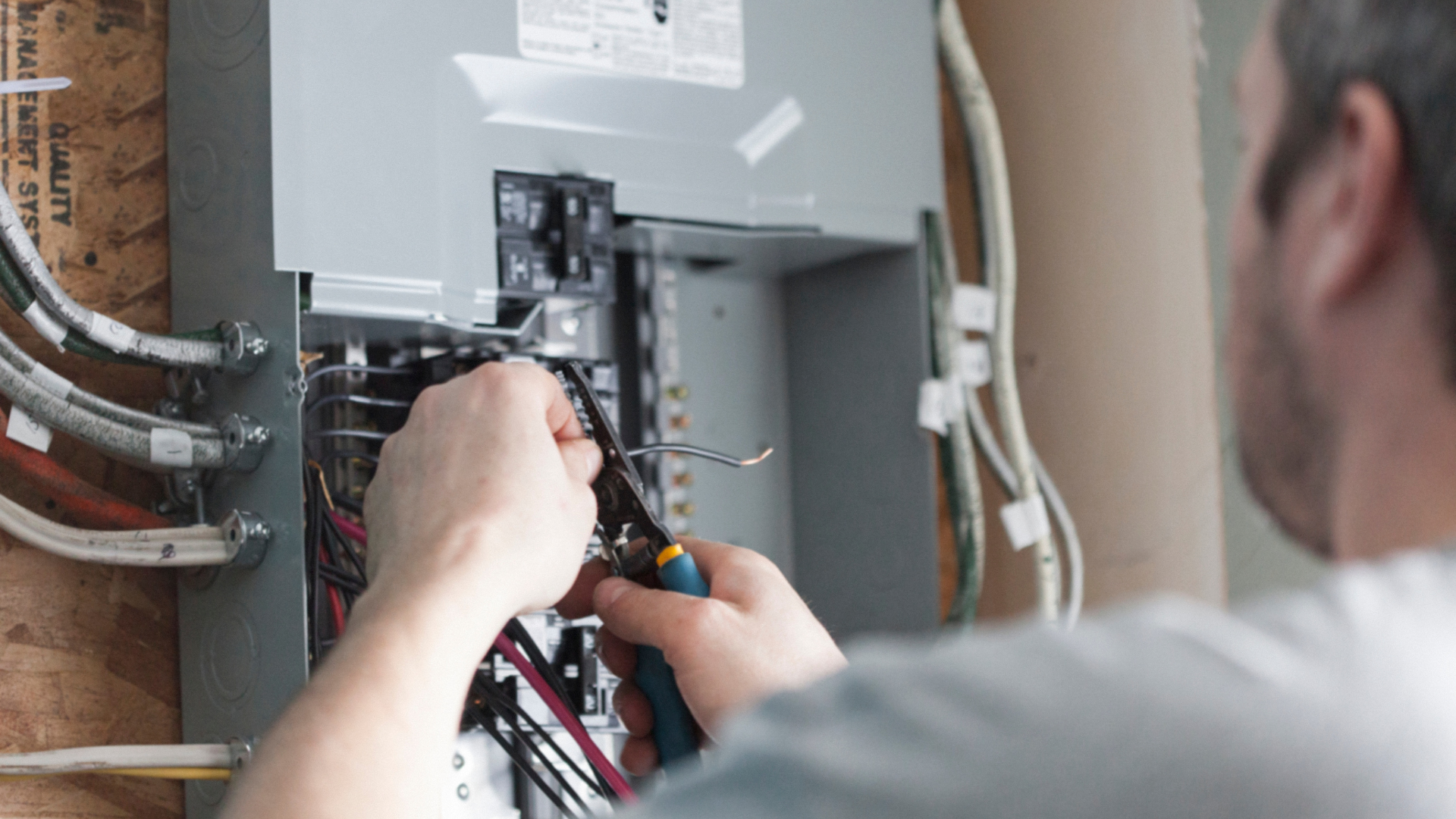 Man wiring an electrical panel with wire cutters, indoors.