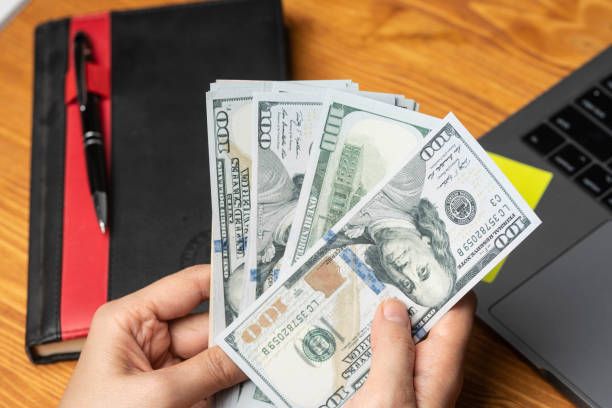 Hands holding a stack of $100 bills on a wooden desk