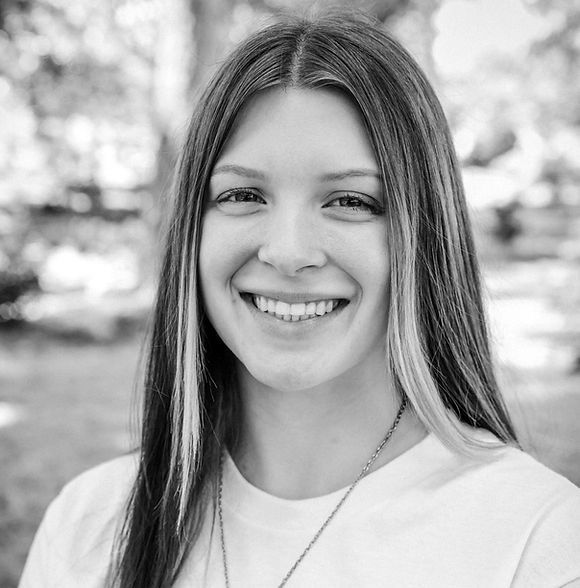 Woman with long hair smiles, wearing a white t-shirt, outdoors.